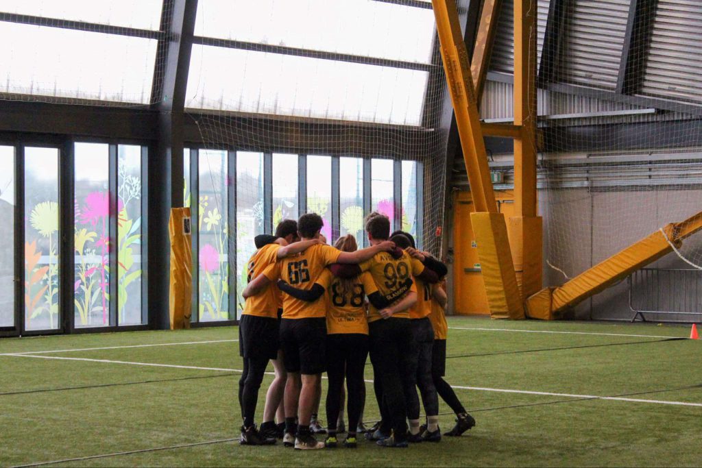 FarFlung players huddling together on an indoors pitch. 