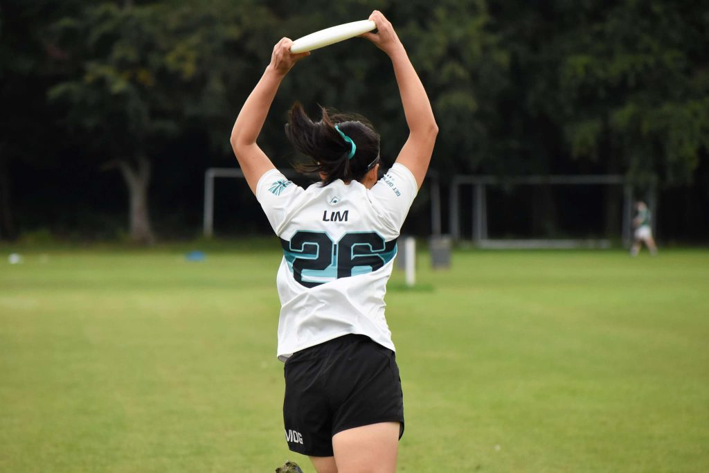 A picture of Natasha from the back showing her catching a disc with her arms up in the air. Her Smog number 26 is visible.